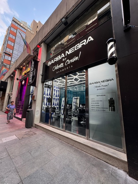 Exterior of Barba Negra barbershop, featuring sleek signage and modern decor, with a passerby on the bustling street.