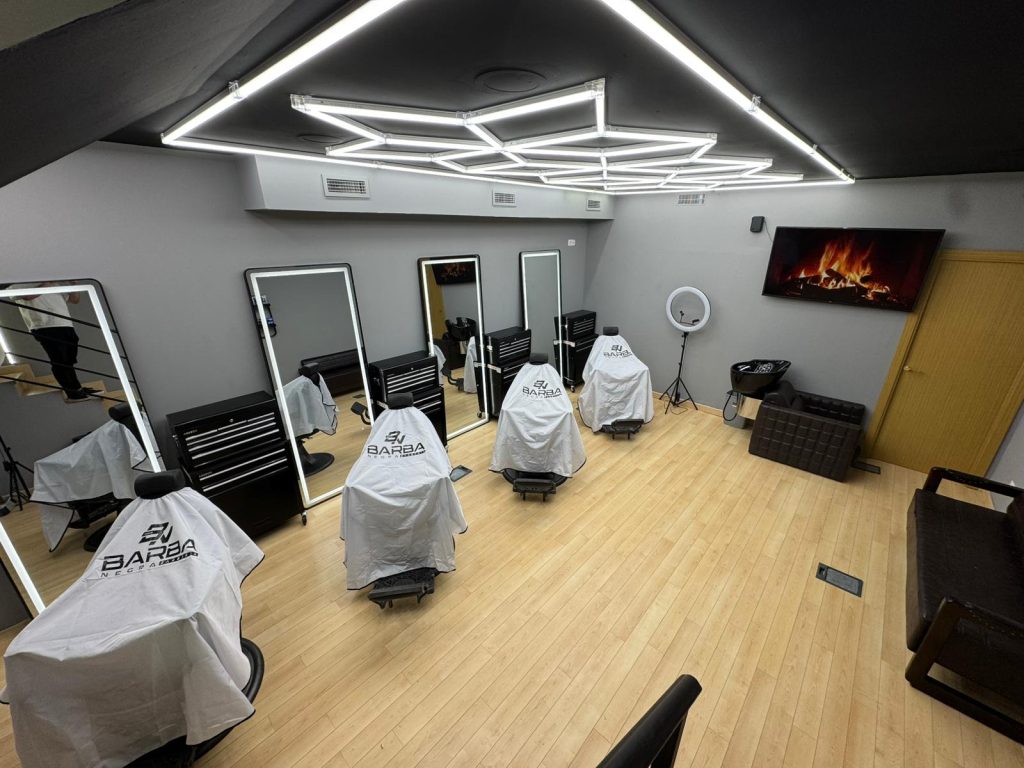 A modern barber shop interior with stylist chairs, mirrors, and a cozy electric fireplace on the wall, featuring sleek lighting.